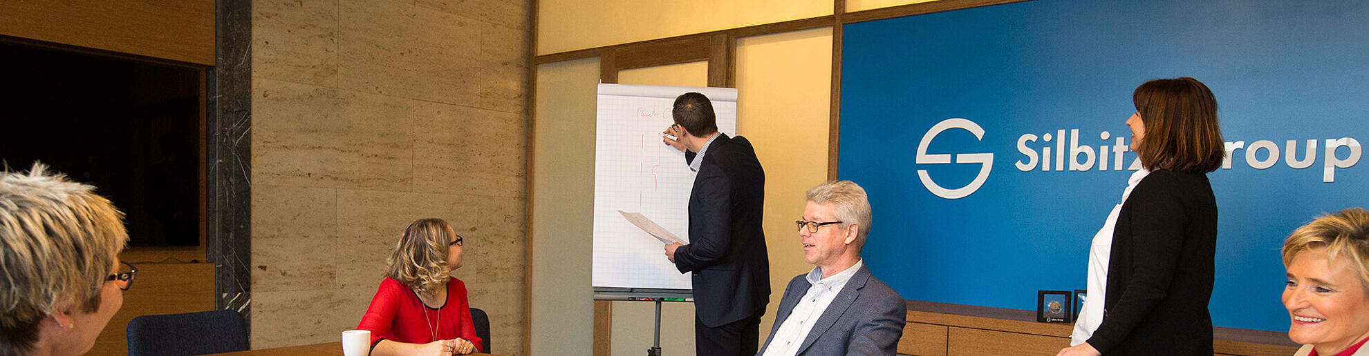 Mehrere Personen sitzen bei einem Meeting zusammen und besprechen diverse Themen.