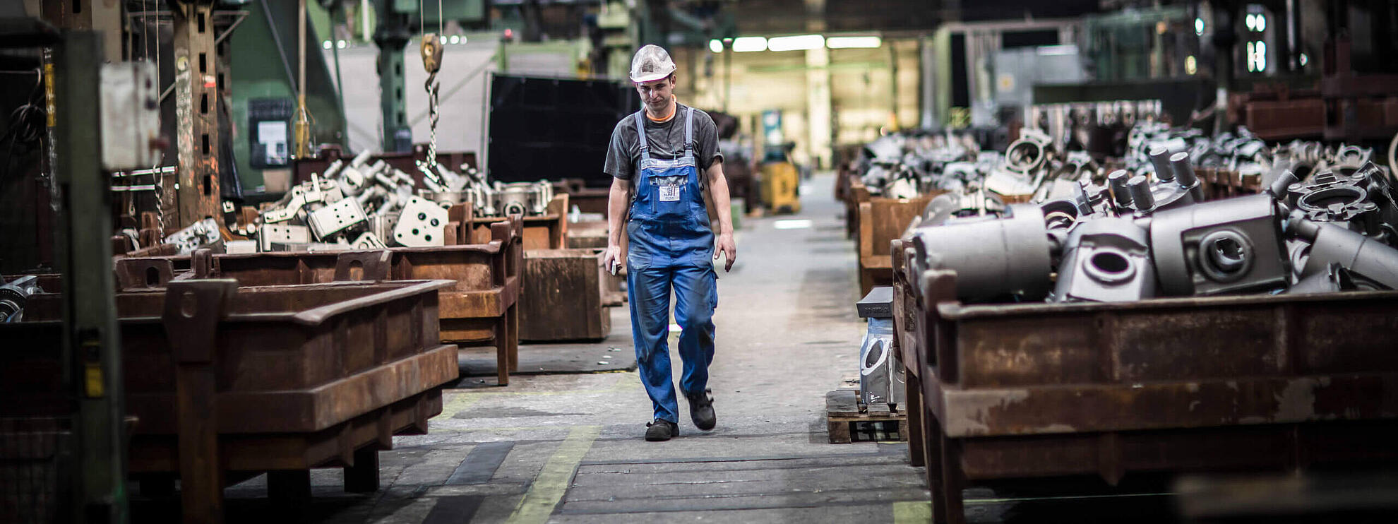 Ein Mitarbeiter steht in einer Lagerhalle voll mit neu angefertigten Bauteilen