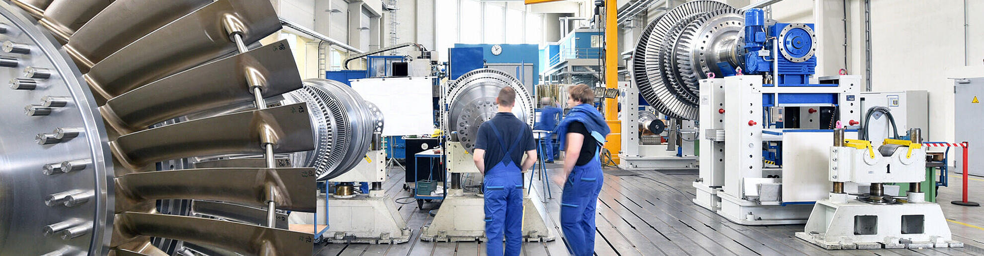Zwei Angestellte stehen in einer langen Halle gefüllt mit diversen Maschinen für Energietechnik.